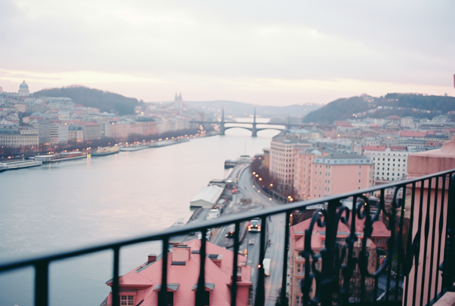 A city river at dusk lined with pastel buildings and crossed by a bridge.