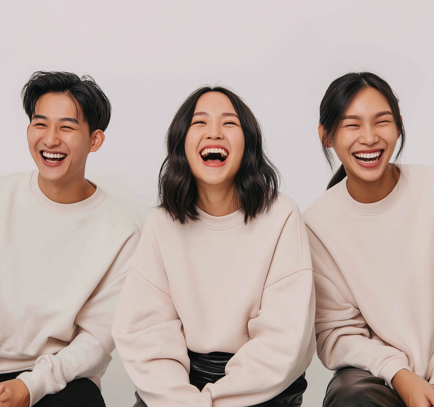 Three friends in light sweatshirts laughing together side by side.